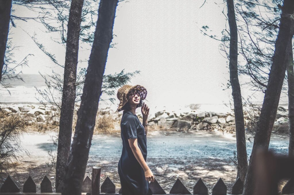 A young woman poses stylishly by a lakeside in Đắk Ya, Vietnam, surrounded by trees.