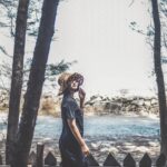 A young woman poses stylishly by a lakeside in Đắk Ya, Vietnam, surrounded by trees.