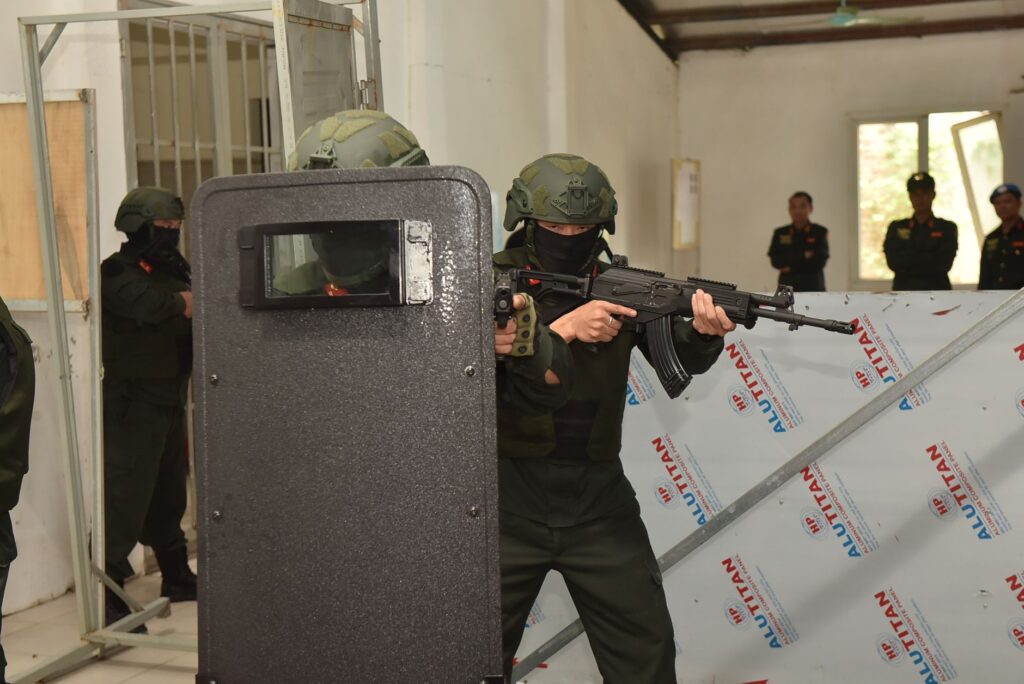 Armed security personnel conducting a tactical training exercise indoors with shields and weapons.