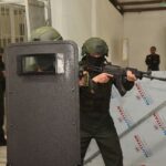 Armed security personnel conducting a tactical training exercise indoors with shields and weapons.