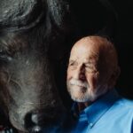 Portrait of an elderly man contemplating beside a buffalo, evoking a sense of connection and reflection.