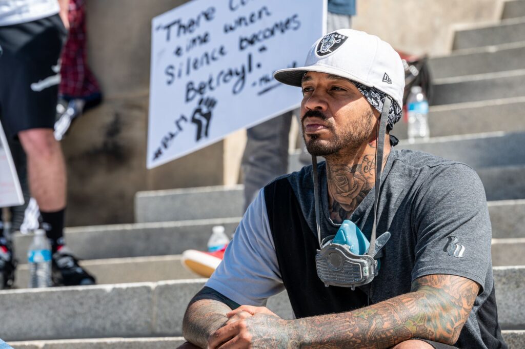 Thoughtful young tattooed African American male activist in trendy outfit sitting on stairs on street and looking away pensively during Black Lives Matter demonstration