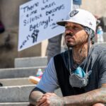 Thoughtful young tattooed African American male activist in trendy outfit sitting on stairs on street and looking away pensively during Black Lives Matter demonstration