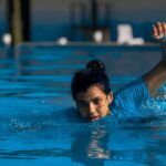 A woman swims energetically in an outdoor pool, enjoying a sunny day.