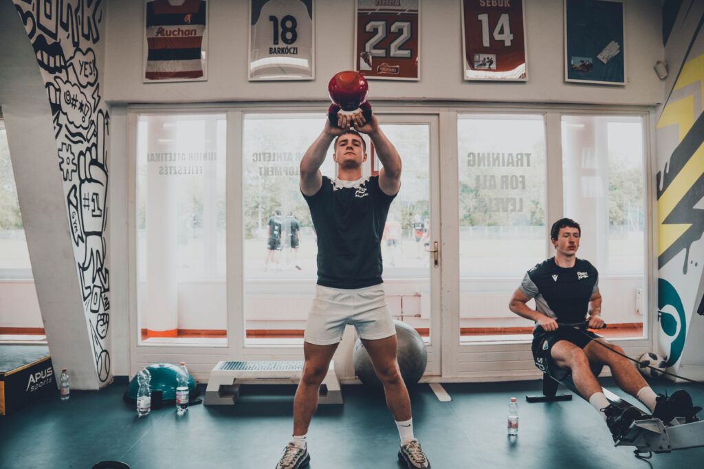 Two young men working out in a gym, focusing on strength training with kettlebells.