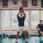 Two young men working out in a gym, focusing on strength training with kettlebells.