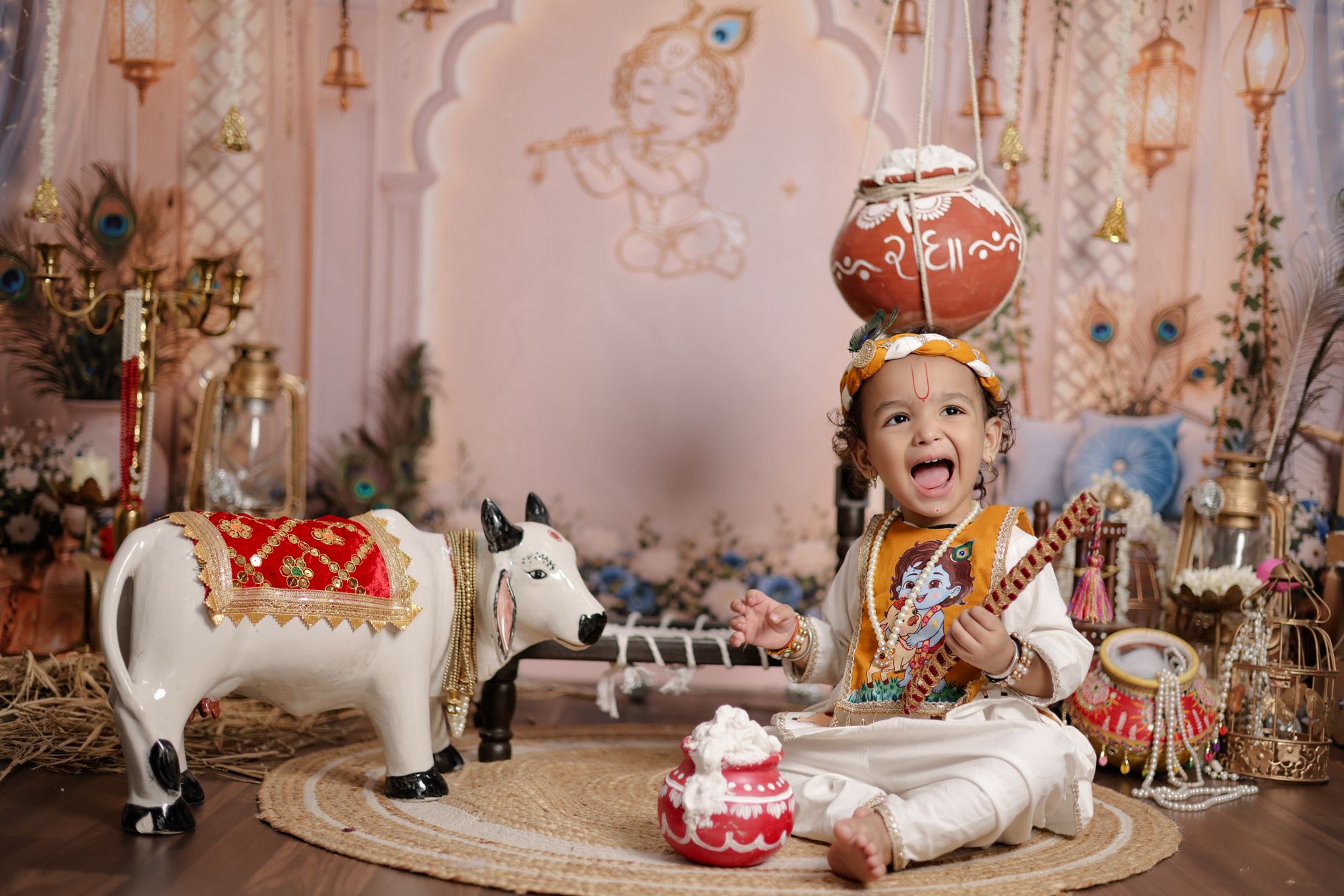 Joyful child in traditional attire with festive decor celebrating Janmashtami indoors.