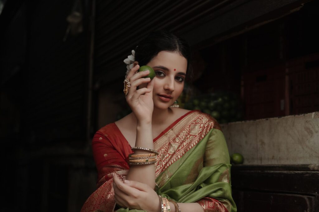A woman in traditional sari holds a lime in a dimly lit market setting, exuding grace.