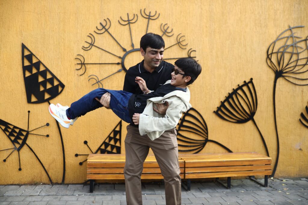 Father lifting son playfully against artistic outdoor mural, showcasing joyful family bonding.