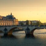 Scenic view of a historic arch bridge in Paris at sunset, showcasing the Seine River with the Musée d'Orsay in the background.