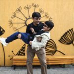 Father lifting son playfully against artistic outdoor mural, showcasing joyful family bonding.