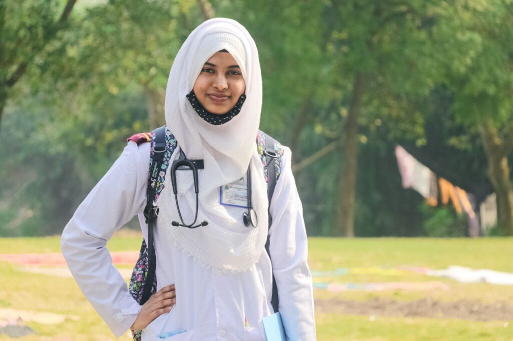 Portrait of a smiling Muslim female doctor wearing a hijab and stethoscope standing outdoors in Dhaka.