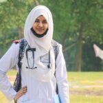 Portrait of a smiling Muslim female doctor wearing a hijab and stethoscope standing outdoors in Dhaka.