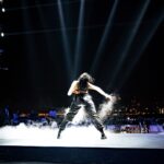 A powerful back view of a performer on stage with dramatic city skyline at night.
