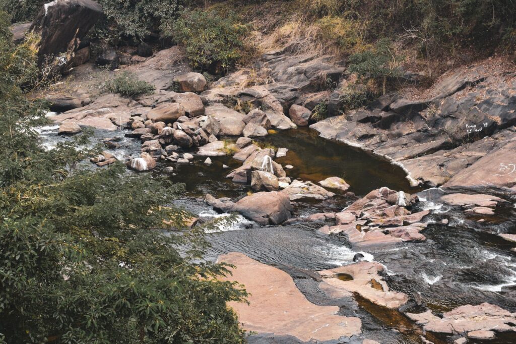 Peaceful stream flowing through rocky terrain with surrounding greenery and eroded stones.