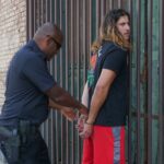 Police officer handcuffing a suspect during an arrest against an urban backdrop.