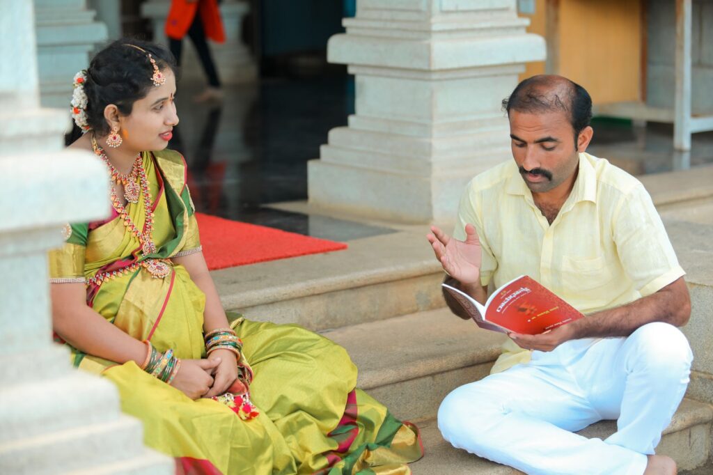 A man and woman in traditional attire reading a book on steps, sharing knowledge.