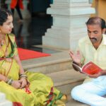 A man and woman in traditional attire reading a book on steps, sharing knowledge.