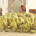 A group of women in hijabs sitting on the mosque's tiled floor, engaged in prayer.