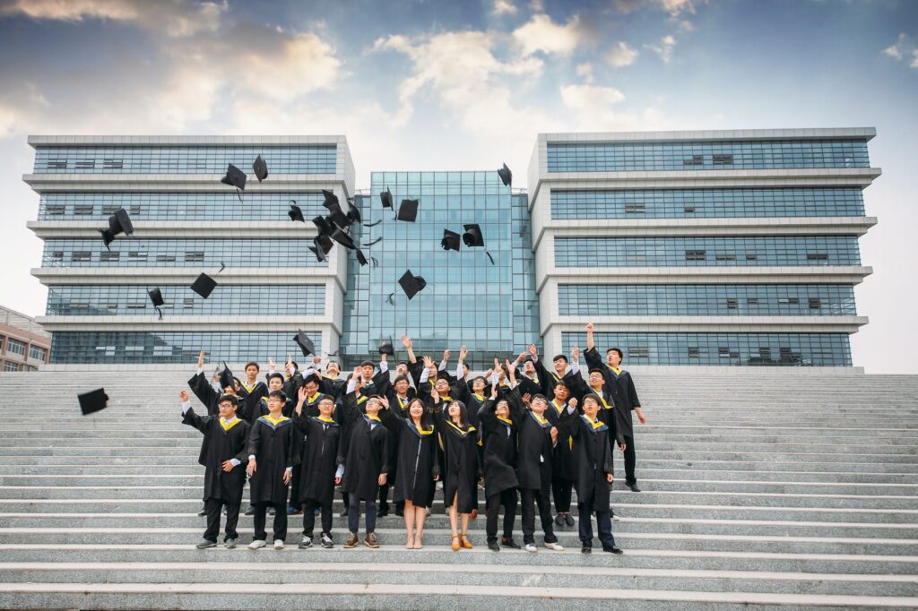 Group of graduates celebrating and tossing caps outside modern building.