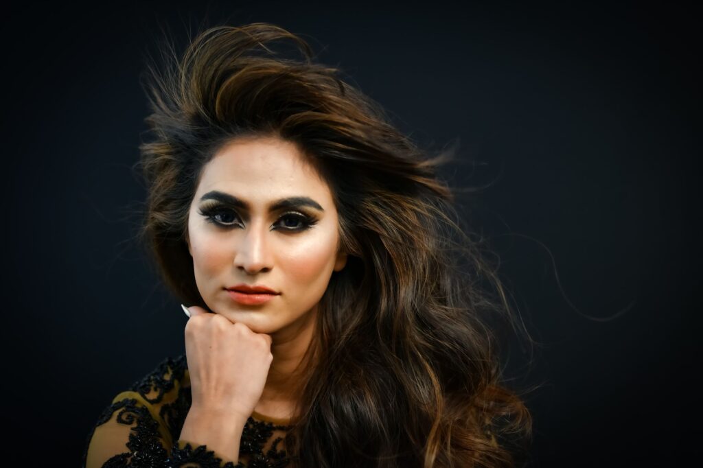 Stunning portrait of a woman with striking eye makeup and red lipstick against a dark background.