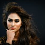Stunning portrait of a woman with striking eye makeup and red lipstick against a dark background.