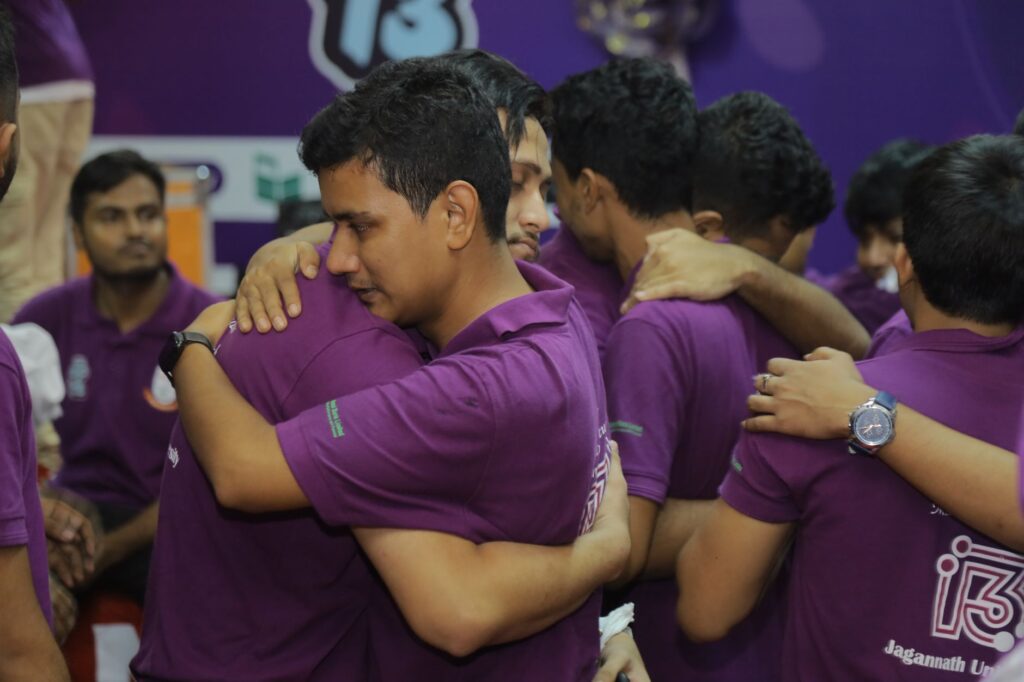 Men in purple shirts hugging, showcasing teamwork and unity at a sports event.