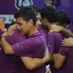 Men in purple shirts hugging, showcasing teamwork and unity at a sports event.