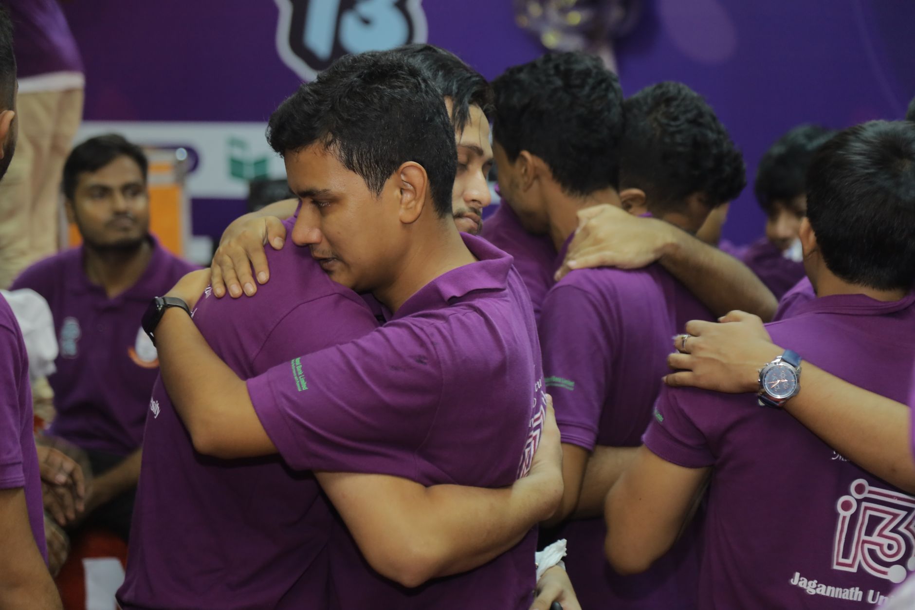 Men in purple shirts hugging, showcasing teamwork and unity at a sports event.