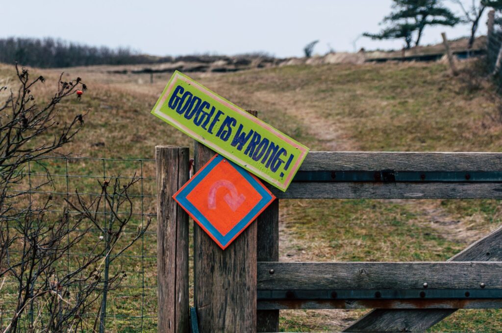 A wooden gate with humorous signs set in a rural landscape, expressing playful dissent.