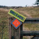A wooden gate with humorous signs set in a rural landscape, expressing playful dissent.