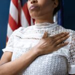 A confident woman in white lace dress pledges allegiance, symbolizing leadership and patriotism.