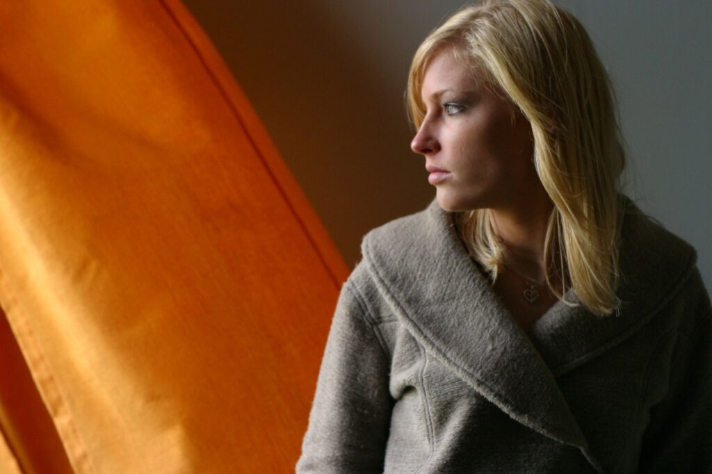 A thoughtful woman in warm light gazes outside, conveying introspection.