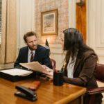 Two professionals engaged in a business discussion in an office setting, reviewing legal documents.