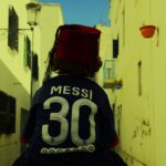 Back view of a person on a Tunis street wearing a fez and Messi jersey.
