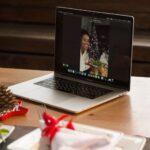 Laptop displaying a festive video call, showing a holiday dinner setting.
