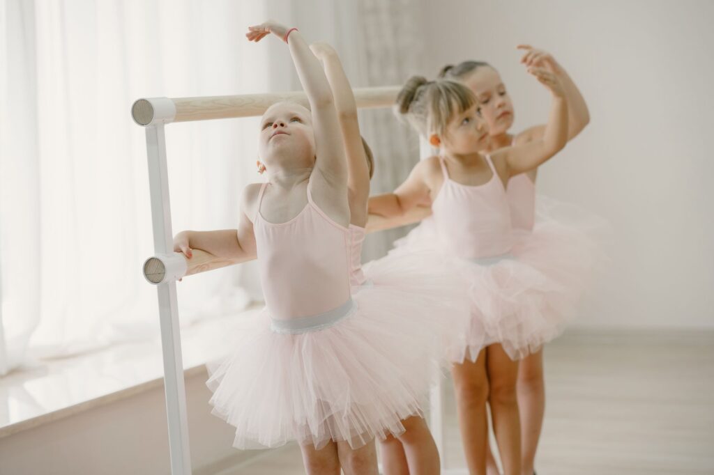 Three young girls in tutus practice ballet at the barre in a bright studio.