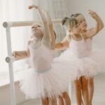 Three young girls in tutus practice ballet at the barre in a bright studio.
