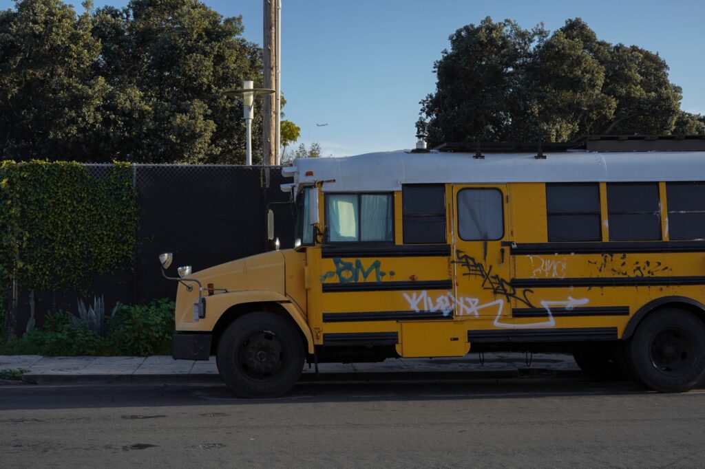 A vintage yellow school bus with graffiti parked on a street in Los Angeles, CA.