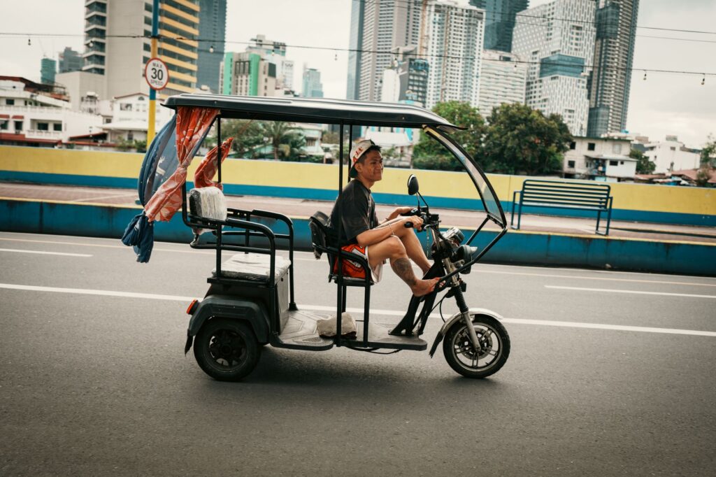 Man riding an electric tricycle on the street in Mandaluyong, with skyscrapers in the background.