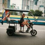 Man riding an electric tricycle on the street in Mandaluyong, with skyscrapers in the background.