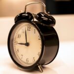 Close-up of a classic black analogue alarm clock on a desk with a serene background.