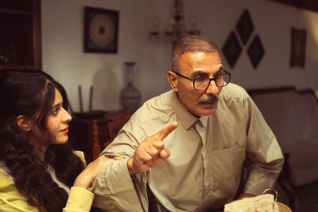 An older man and young woman having an intense discussion in a cozy living room setting.