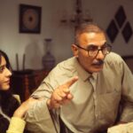 An older man and young woman having an intense discussion in a cozy living room setting.