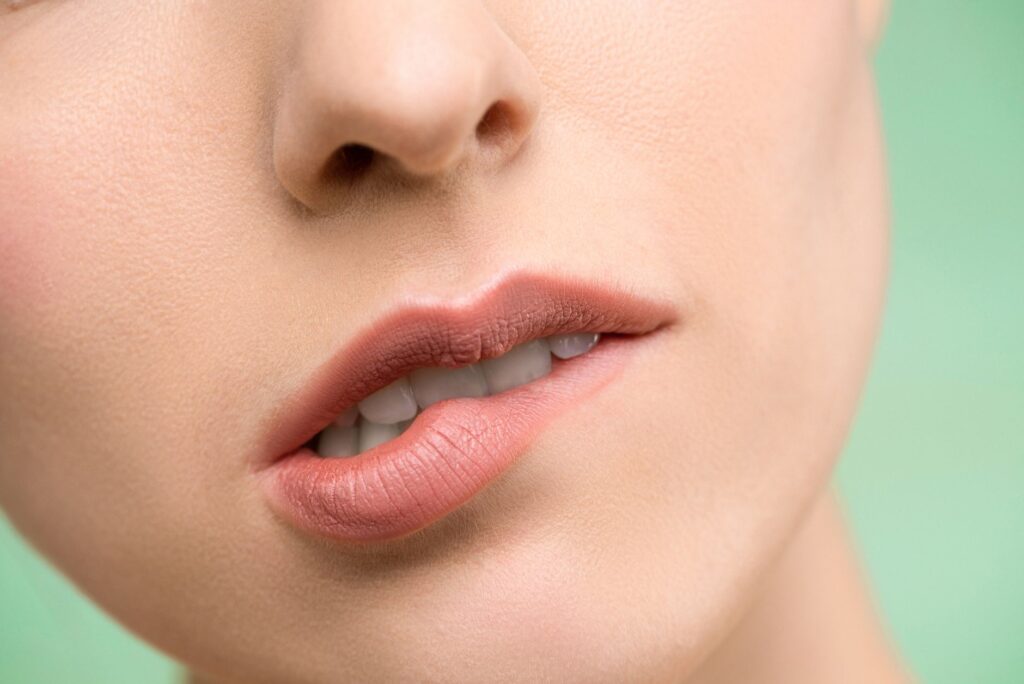 A close-up image showcasing a woman's lips with natural makeup against a pastel background.