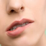 A close-up image showcasing a woman's lips with natural makeup against a pastel background.