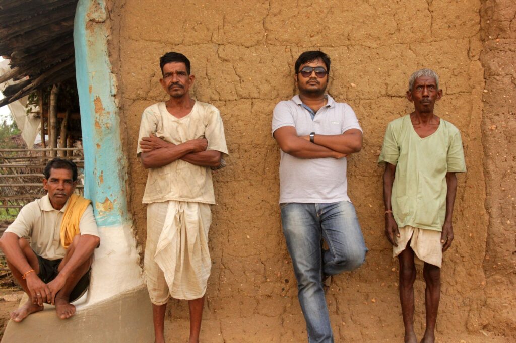 Four men standing and sitting against a mud wall in Balaghat, India.