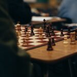 High angle of crop anonymous people sitting at table and playing chess in club