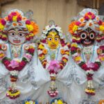 Vibrant Jagannath, Balabhadra, and Subhadra idols adorned with flowers and ornaments indoors.