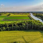 Aerial view of green farmland and river under a clear blue sky, showcasing vibrant agricultural landscapes.